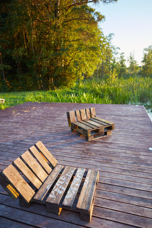 Wooden deck chairs on a wooden pier in the forest at sunset