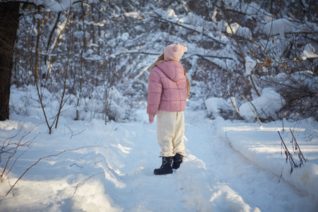 Little girl walking in the winter forest. The child is dressed in a pink jacket and white pants.の写真素材