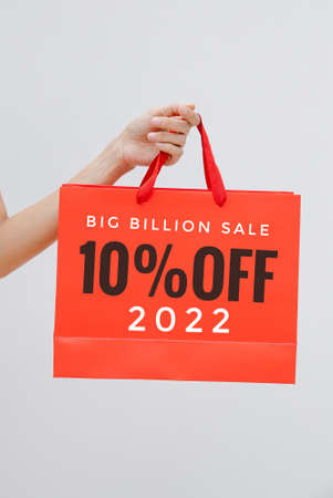 Woman hand holding red shopping bag with inscription on white background