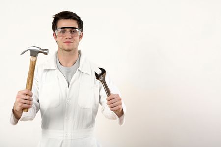 Man with safety goggles holding a hammer and adjustable spanner in each handの写真素材