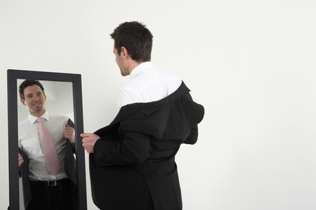 Businessman standing in front of the mirror wearing his coatの写真素材