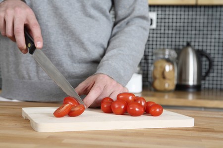 Man cutting cherry tomatoes in the kitchenの写真素材