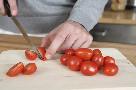 Man cutting cherry tomatoes in the kitchenの写真素材