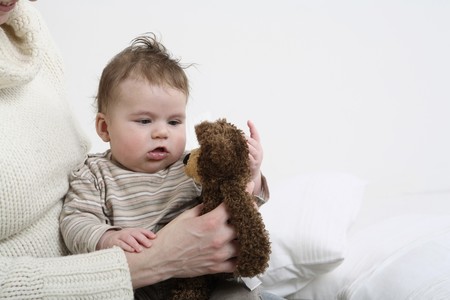 Baby playing with soft toy held by womanの写真素材