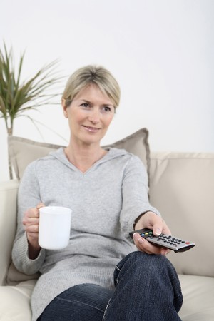 Woman holding a cup of coffee while changing channel