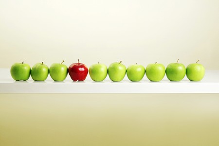 Red apple among a row of green apples