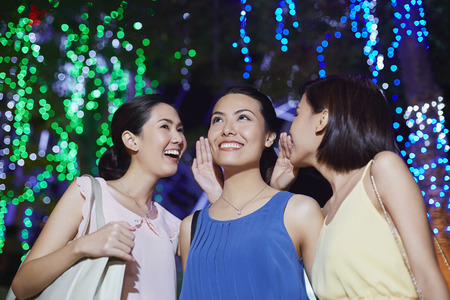 Two young women whispering to their friendの写真素材