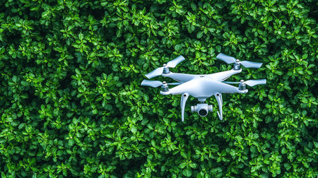 Drone quadcopter with digital camera flying over green leaves backgroundの素材