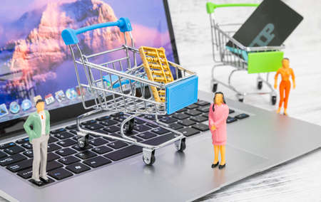 A shopping cart and a small person model on a laptopの写真素材