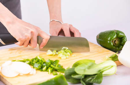 Hands chopping vegetables on wooden cutting board