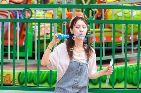 Beautiful oriental girl playing with blowing bubbles in amusement parkの写真素材