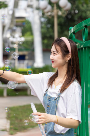 Beautiful oriental girl playing with blowing bubbles in amusement parkの写真素材
