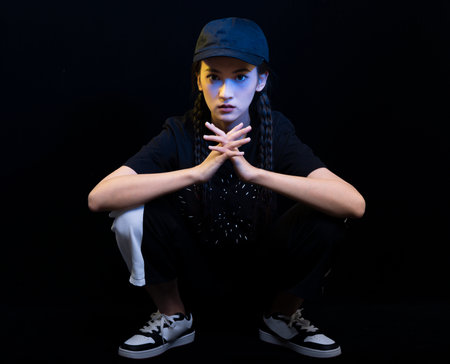 Portrait of a beautiful girl with braids in a cap and a T-shirt on a black backgroundの写真素材