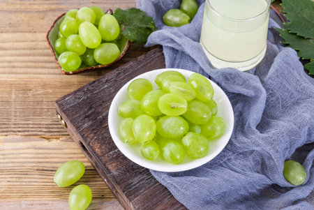 Fresh green grapes in bowl and glass of grape juice on wooden backgroundの写真素材