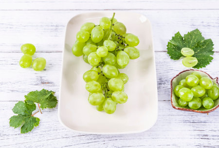 Bunch of green grapes on a white plate on a wooden backgroundの写真素材
