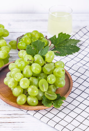 Green grapes in a wooden plate on a white wooden background. Selective focus.の写真素材