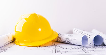 Yellow hard hat and rolls of blueprints on the office desk.の写真素材