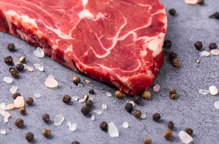 Raw beef steak with salt and peppercorns on a stone background.の写真素材