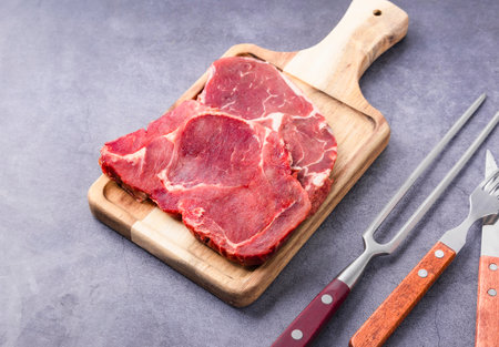 Raw fresh beef steak on wooden cutting board with fork and knife.の写真素材