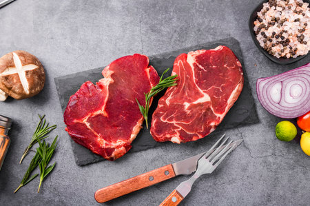 Raw beef steaks with ingredients for cooking on a stone background.の写真素材
