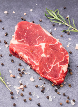 Raw beef steak with rosemary and peppercorns on a stone backgroundの写真素材