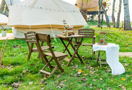 Wooden table and chairs on the lawn in front of a tentの写真素材