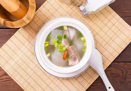 Chinese soup with pork and vegetables in a white bowl on a wooden tableの写真素材