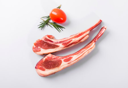 Raw pork ribs with rosemary and tomatoes on a white background.の写真素材