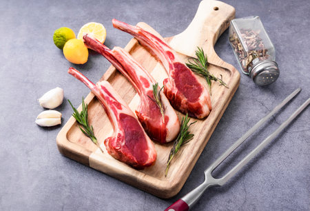 Raw fresh lamb chops with rosemary, garlic and pepper on wooden cutting boardの写真素材
