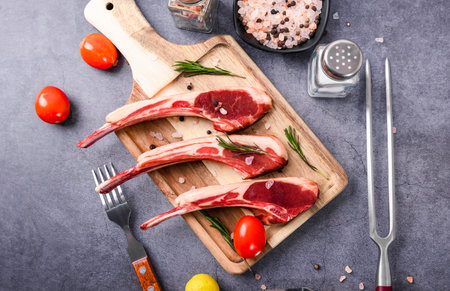 Raw fresh lamb chops with spices and herbs on wooden cutting board.の写真素材