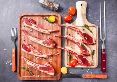 Raw lamb chops on wooden cutting board with rosemary, spices and vegetables.の写真素材