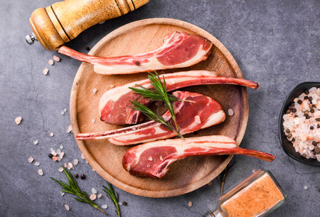 Raw lamb chops with rosemary, salt and pepper on wooden cutting boardの写真素材