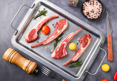 Raw lamb chops with rosemary, salt and pepper on metal tray.の写真素材