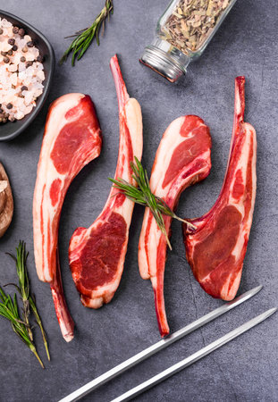 Raw lamb chops with rosemary and spices on a stone background.の写真素材
