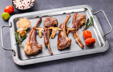 Grilled lamb chops with mushrooms and vegetables on a metal tray.の写真素材