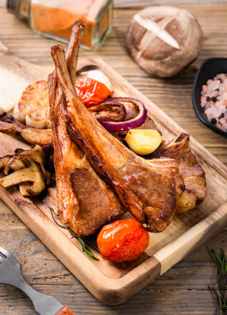 Grilled lamb chops with baked potatoes and vegetables on a wooden boardの写真素材