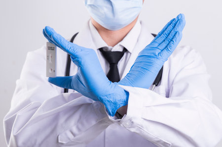 Doctor in a white coat and blue latex gloves shows stop gesture.の写真素材