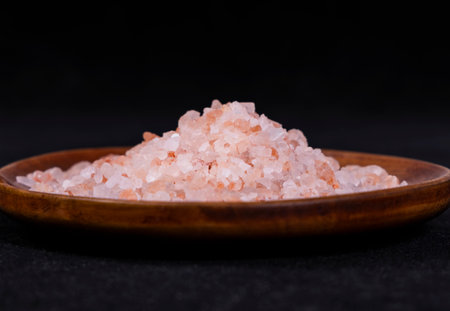 Himalayan pink salt in a wooden bowl on black background.の写真素材