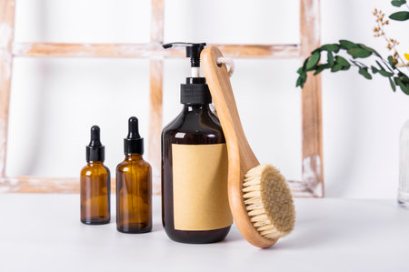 Cosmetics bottles with wooden brush on white table near window in bathroomの写真素材