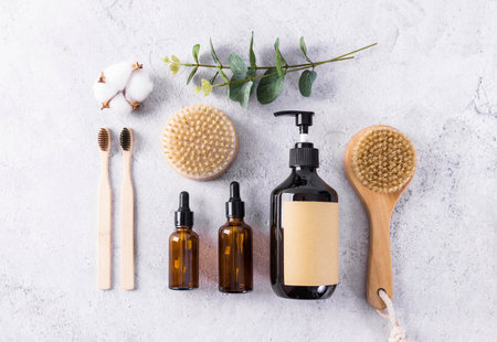 Eco friendly zero waste bathroom accessories. Natural bamboo toothbrushes, glass bottles with cosmetic products and eucalyptus branch on white background.の写真素材