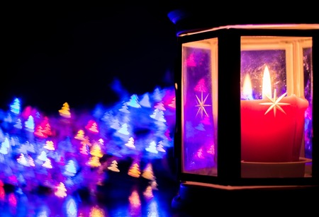 Lantern with burning candle on the right side on the background of colorful bokeh in the form of Christmas treesの写真素材