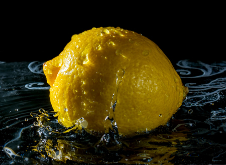 Lemon in water with reflection from water splashes on black backgroundの写真素材