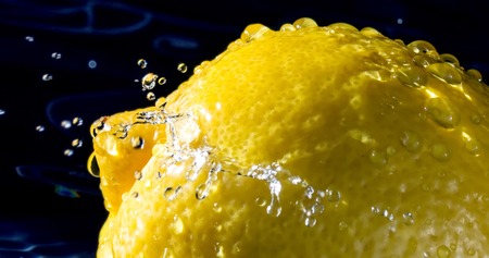 Lemon with splashes falling drops of water close up macro on black backgroundの写真素材