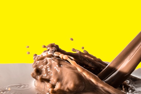 Splash of chocolate, pouring stream of chocolate, cocoa, isolated on yellow backgroundの写真素材