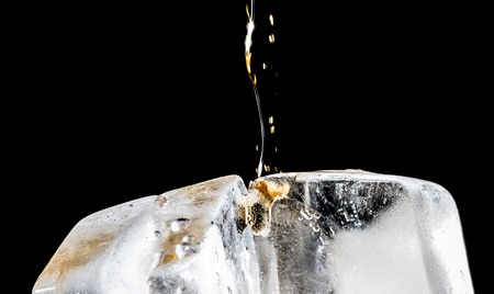 Stream of soda being pouring into a glass with soda and ice cube on black background, closeup texture, splashing, splash, fizzの写真素材
