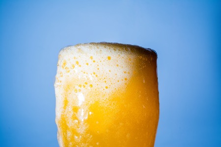 Orange soda large glass, overflowing glass of orange soda closeup with bubbles on blue backgroundの写真素材