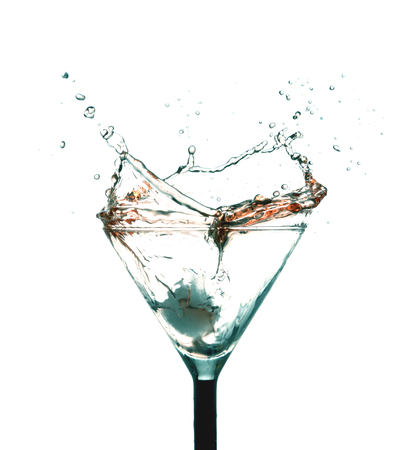 Ice cubes splashing in glass of alcohol and many drops and wave on table on white backgroundの写真素材