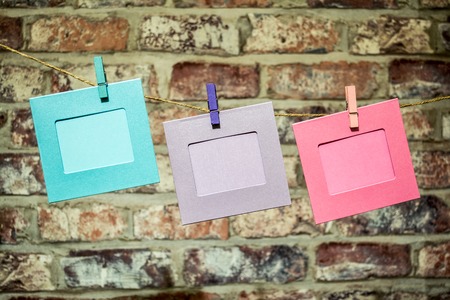 Colorful funny picture frames hanging on a rope with clothespins twine on the old, vintage brick wall backgroundの写真素材