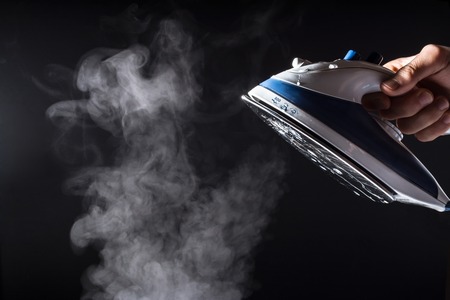 Hand holds an iron with steam and water stream isolated on a black backgroundの写真素材