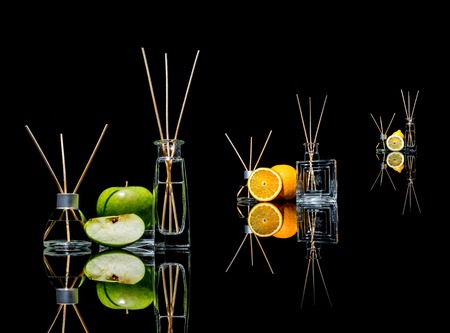 Air fresheners in a glass jars with sticks and lemon, green apple and orange with reflection...